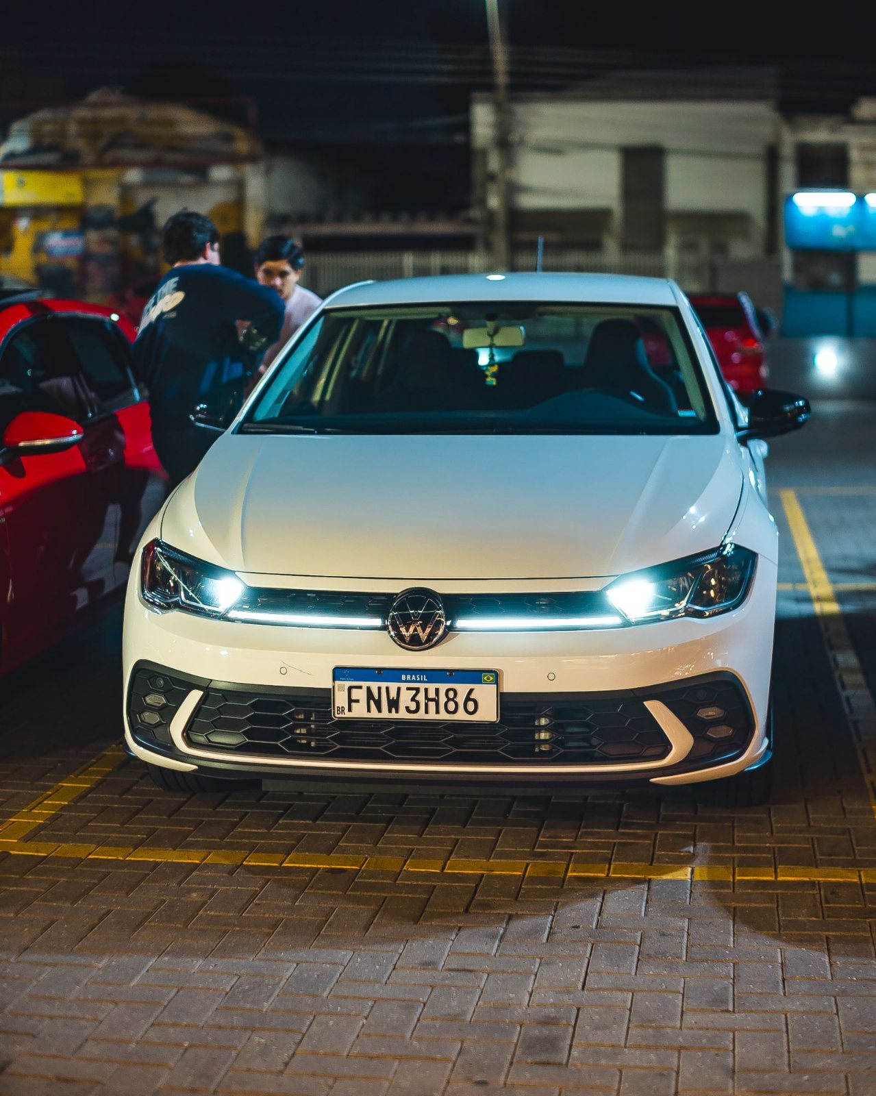 Volkswagen Polo branco com faróis acesos num rolê noturno do clube